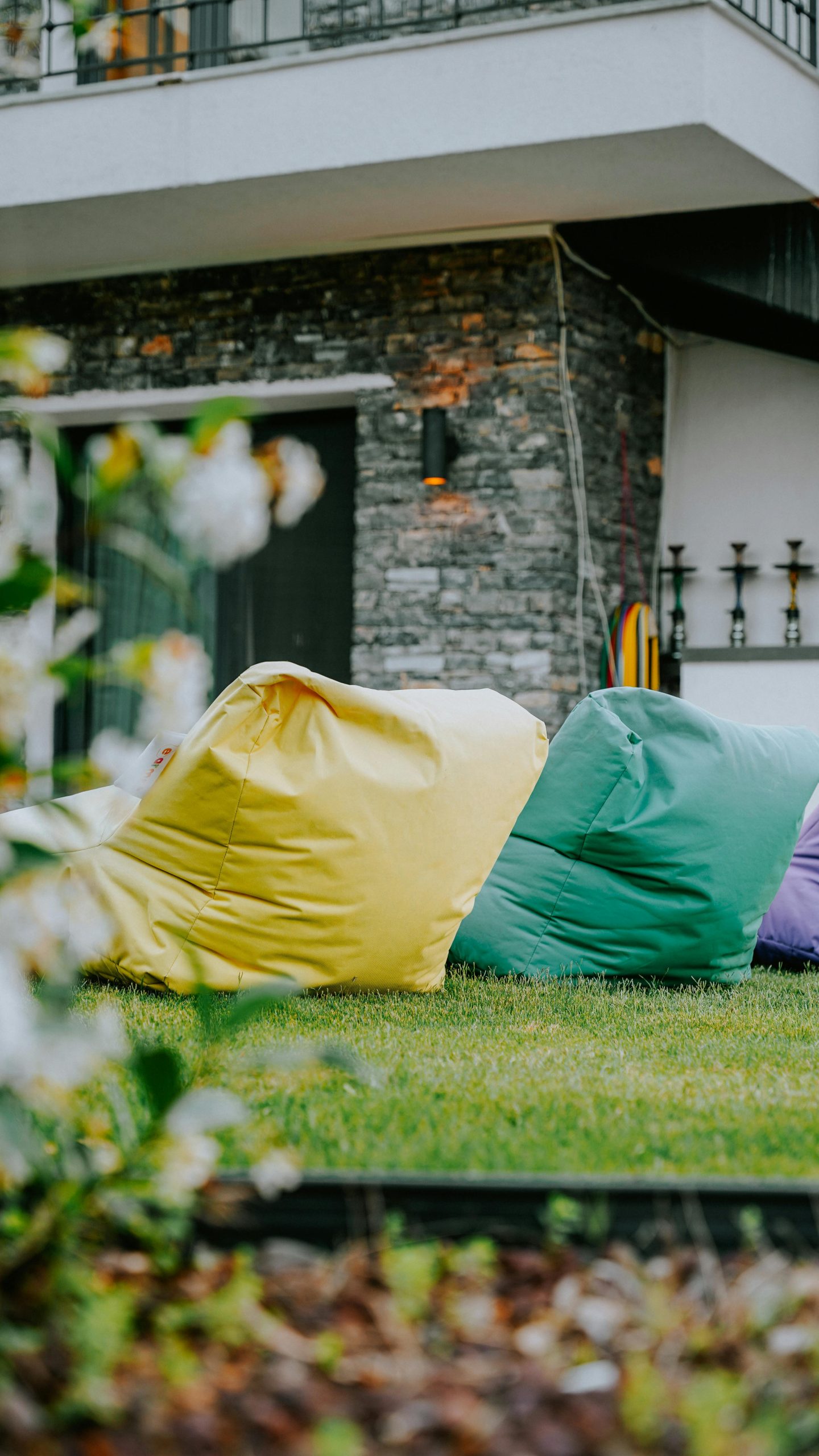 Vibrant bean bags on a garden lawn in front of a modern house with stone walls.